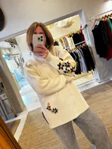Sweater de punto color beige con cuello alto, mangas largas y corte holgado. Presenta tajos laterales y bordados florales en puños y cadera.