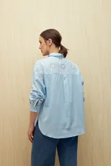 Camisa celeste de manga larga con cuello camisero y botones de nácar. Presenta detalles de broderie calado en el canesú y las mangas.