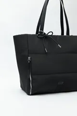 Bolso tote negro de nylon con diseño acolchado, asas largas para llevar al hombro, cierres metálicos laterales y detalle de cordón.