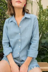 Camisa celeste de lino con cuello clásico, manga larga con puños abotonados, cierre frontal con botones y bolsillo en el pecho. Presenta bordado floral en la espalda.