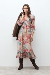 Vestido largo de manga larga, con escote en V y fruncido bajo el busto. Presenta un estampado tipo paisley en tonos rojo, azul claro y beige. El ruedo termina con un volante fruncido.