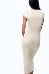 Vestido midi color beige confeccionado en hilatura con algodón. Tiene cuello redondo, manga corta caída y detalle de drapeado lateral.
