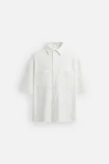 Sobrecamisa blanca de tejido elástico, con cuello solapa, manga corta y bolsillos de plastrón en el pecho. Cierre frontal con botones a presión.