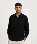 Camisa negra de lino con corte clásico, cuello camisero y mangas largas. Cierre frontal con botones.