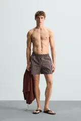 Bañador corto de hombre con estampado de rayas verticales en marrón, blanco y azul. Cuenta con cintura elástica ajustable con cordón, bolsillos laterales y trasero.