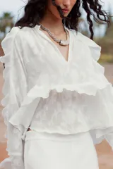 Camisa blanca de cuello redondo con escote en V y mangas largas acampanadas con volantes.