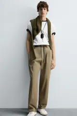 Pantalón color caqui de corte tapered relaxed fit, confeccionado en tejido de algodón. Presenta cintura con pliegues frontales dobles, bolsillos laterales en cadera y bolsillos traseros de vivo con botón. Cierre frontal con cremallera y botón.