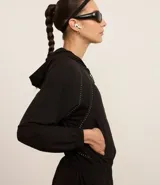 Campera deportiva cropped color negro, con capucha y mangas largas. Presenta cierre frontal, detalle reflectante y está confeccionada en tejido tecnológico.