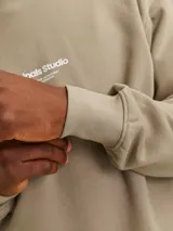 Buzo color arena de manga larga y cuello redondo, con logo "Originals Studio" estampado en el pecho.