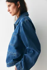 Campera azul de denim con cuello clásico, cierre frontal con botones dorados, dos bolsillos de parche en el pecho y dos bolsillos ribeteados en la cintura.
