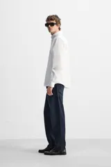 Camisa blanca de corte regular fit confeccionada en popelín de algodón. Tiene cuello abotonado, manga larga con puños abotonados y cierre frontal con botones.