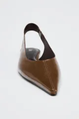Zapato tipo bailarina destalonada en piel color marrón. Detalle de pespunte en el corte. Tira trasera con elástico lateral. Acabado en punta. Suela plana.