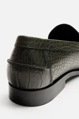 Mocasín de vestir color marrón oscuro con grabado tipo cocodrilo, horma redonda y suela con ligero tacón.