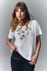 Remera negra de algodón con cuello redondo y mangas cortas. Presenta un estampado en el escote que simula un collar estilo boho con cuentas, borlas y dijes.