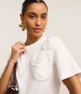 Blusa blanca de algodón con cuello redondo, mangas cortas y apliques de flores de tela en el hombro.