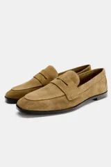 Zapato plano tipo mocasín color marrón claro, confeccionado en piel de serraje. Tiene copete subido, antifaz y punta redonda.