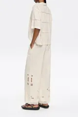 Pantalón de lino color crema, de corte palazzo y tiro alto, con bolsillos laterales y bordados en el ruedo.