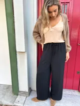 Pantalón negro de seda opaca, corte palazzo, tiro medio alto y cintura elástica con cordón ajustable.