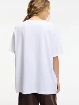 Remera blanca de algodón con cuello redondo y mangas cortas, decorada con apliques de brillantes plateados de diferentes tamaños en el frente.