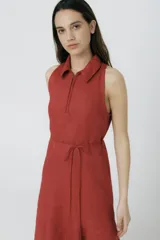 Vestido largo color ladrillo, sin mangas, con cuello camisero, cierre frontal con cremallera y lazo ajustable en la cintura.