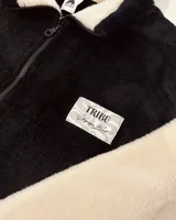 Campera de peluche negra con mangas blancas, cierre frontal y cuello alto.