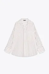 Camisa blanca con rayas verticales grises, de corte holgado, cuello solapa y mangas largas con puños abotonados. Tiene un bolsillo de parche en el pecho, pinzas en la espalda y bajo asimétrico con aberturas laterales.