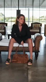 Cartera tipo tote bag color marrón, de gamuza, con cierre superior y doble asa de hombro.