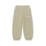Pantalón de jogging color beige, de corte oversize, con cintura y puños elásticos. Presenta un pequeño texto bordado en blanco en la parte superior del muslo derecho.