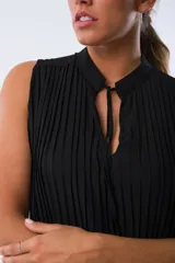 Blusa negra sin mangas con cuello mao y detalle de lazos en el escote. Diseño plisado en todo el cuerpo.