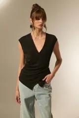 Top negro sin mangas, con escote en V cruzado y detalle de botones laterales. Presenta un corte ajustado al cuerpo con un diseño asimétrico en el ruedo.