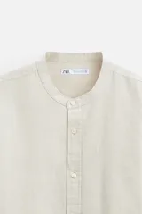 Camisa color beige claro, de corte relaxed fit, confeccionada en tejido de lino y algodón. Tiene cuello mao, manga larga con puños abotonados y cierre frontal con botones.