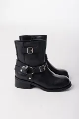 Bota corta de cuero negro con hebillas y arneses metálicos.