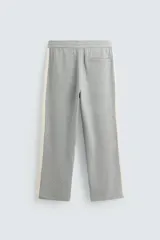 Pantalón de jogging gris con corte relaxed fit, cintura elástica ajustable con cordón interior, bolsillos laterales y traseros de vivo, y banda lateral color crema.
