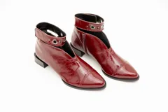 Botín de cuero color borgoña con taco bajo, corte en V en el empeine, pulsera con detalles metálicos y cierre lateral.