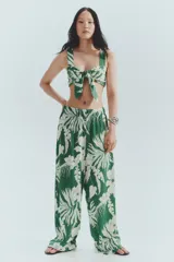 Pantalón ancho de punto con estampado floral blanco sobre fondo verde. Tiene tiro alto, cintura elástica y piernas amplias.