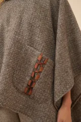 Poncho de lana color marrón con cuello alto, mangas 3/4 y bolsillo lateral con detalle de botones de cuero.