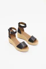 Sandalia de cuero vacuno color negro con taco tipo cuña revestido en yute. Presenta una tira ancha sobre el empeine y una pulsera ajustable al tobillo con cierre de hebilla metálica.