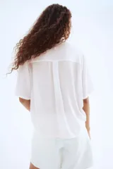 Camisa blanca de viscosa con efecto arrugado, de manga corta, corte holgado, cuello clásico, botones frontales y canesú con pliegue de caja en la espalda.