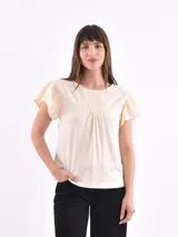 Remera color blanco hueso con mangas cortas con volados y detalle de bordado inglés en el canesú superior y en los bordes de las mangas. Presenta un frunce central en el pecho.