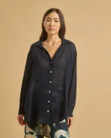 Camisa azul marino de manga larga con botones blancos, corte fluido y largo asimétrico.