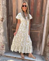 Vestido largo estampado con flores blancas sobre fondo dorado, con mangas cortas con volados y escote en V.