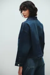 Chaqueta de jean azul oscuro con cuello clásico, cierre frontal con botones metálicos, un bolsillo de parche en el pecho y detalle de lavado en puños y bajo.