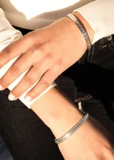 Pulsera esclava abierta de acero quirúrgico color plateado, con diseño de guarda griega.