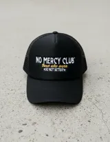 Gorra trucker negra con frente rígido y rejilla trasera. Bordado frontal con la frase "No Mercy Club" en blanco y amarillo.