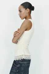 Camiseta ajustada (slim fit) de cuello redondo y manga sisa, color beige claro, con frunces laterales y bajo asimétrico con terminación de encaje a tono.