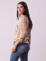 Blusa de gasa estampada a rayas verticales en tonos celeste, lila, naranja y marrón. Tiene cuello a la base con escote en V y botones. Delantera con bolsillo aplicado. Largo de manga regulable con presilla y botón. Terminación anudada opcional.