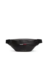 Riñonera negra de poliuretano granulado con cierre de cremallera, correa ajustable de textil trenzado con cierre de apertura fácil, bolsillo interior con cremallera, cinta distintiva y logo metálico de Tommy Hilfiger en la parte delantera.