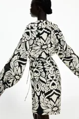 Vestido corto en mezcla de viscosa con estampado floral en blanco y negro, cuello mao fruncido y abertura en V adelante. Modelo de corte holgado con cinturón extraíble para atar en la cintura, y mangas globo largas de corte raglán con abertura y botón en los puños.