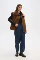 Chaleco marrón de gamuza sintética con cuello y borde de piel sintética. Cierre frontal con cremallera y bolsillos laterales.