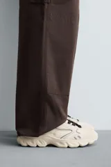 Zapatillas deportivas color crema con cordones, suela gruesa con diseño irregular y detalles en gris.